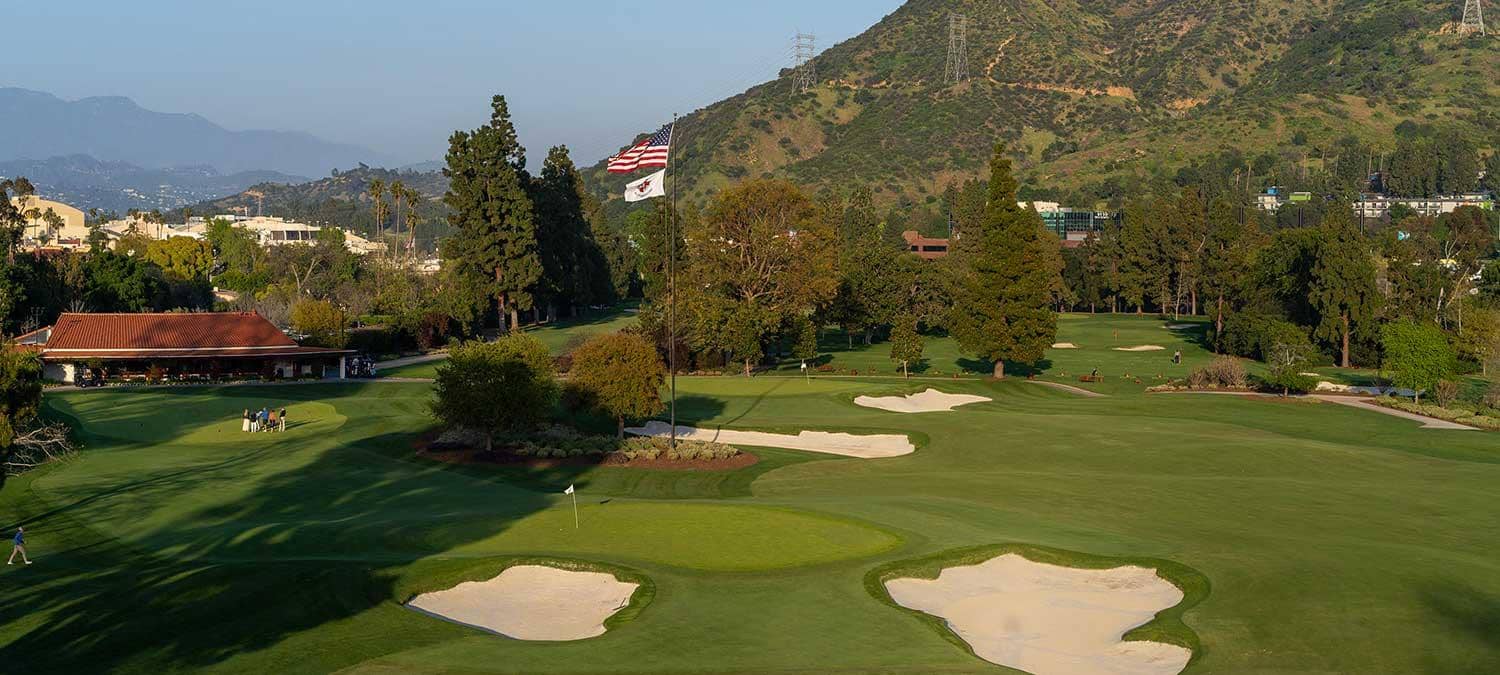 Photo courtesy of Lakeside Golf Club (lakesidegolfclub.com), used for editorial coverage. Green complex, bunkers, clubhouse and flagpole framed by the Verdugo Mountains.
